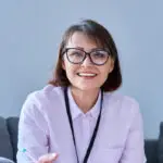 Woman in glasses smiling at desk – therapist brand photo